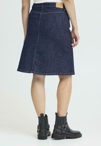 Mörk denim A-linjeformad kjol med en baksidan etikett i midjan, kompletterad med svarta ankelboots med spännen och texturerade paneler.