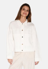 Bijela oversized jakna s dugmadi sprijeda, velikim ovratnikom i dva prednja džepa. Izrađena od mekog materijala s glatkom teksturom.