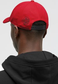 Rote Baseballmütze aus Stoff, mit einem gebogenen Schirm und einem verstellbaren schwarzen Snapback. Auf der Rückseite befindet sich ein Globus-Design mit Text.