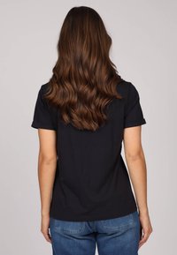 T-shirt en coton noir à manches courtes, coupe décontractée et poignets retroussés, associé à un jean en denim bleu. Vue arrière montrant une texture lisse.