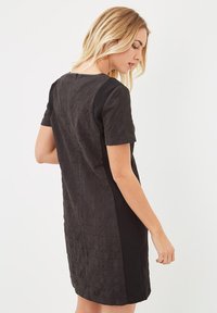 Vestido negro de manga corta con un patrón geométrico texturizado en la espalda y lados negros lisos, con un escote limpio y una silueta ajustada.