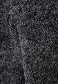 Acercamiento de una tela de lana tejida de color gris oscuro que muestra bucles texturizados y fibras suaves.
