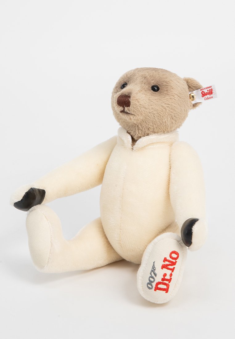 Plüschbär mit beigem Fell, der ein weißes Outfit trägt. Schwarze Pfotenakzente und ein Etikett mit dem 'Steiff'-Logo. Auffälliger gestickter Text "007 Dr. No."