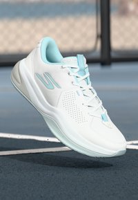 Baskets de sport blanches avec des accents bleu clair, tige en mesh texturé, perforations pour la respirabilité et semelle rembourrée.