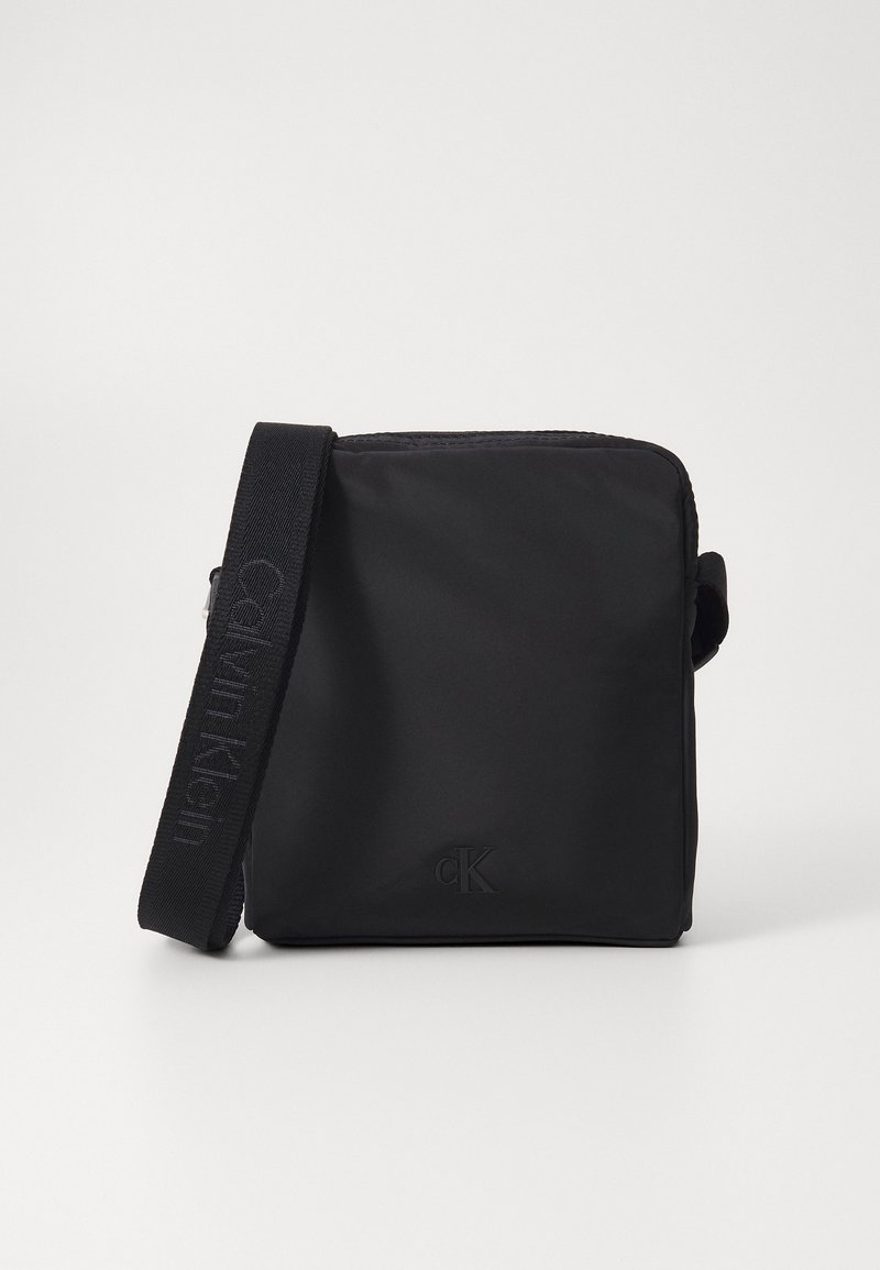 Svart nylon crossover-veske med en glatt tekstur, med "CK"-logo og en justerbar stropp med merkenavnet vevd inn.