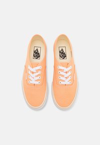 Zapatillas de lona naranjas con cordones blancos, punta redondeada y suela de goma. Presenta un logo en la lengüeta y detalle de costura a lo largo de los bordes.
