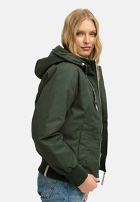 Giacca verde con cappuccio, chiusura con zip frontale, polsini a coste e due tasche laterali. Presenta una texture morbida e una vestibilità comoda.