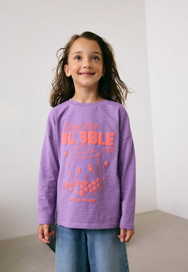 Chemise à manches longues lavande avec un graphique corail représentant une tasse de bubble tea ; comporte le texte "Doux comme le BUBBLE TEA" et "ÉDITION SPÉCIALE."