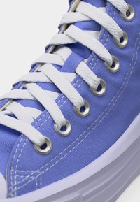 Κοντινό πλάνο μπλε υφασμάτινου αθλητικού παπουτσιού με λευκά κορδόνια περασμένα από ασημένιες μεταλλικές τρύπες και λευκή λαστιχένια σόλα.