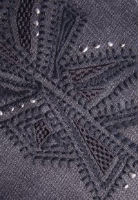 Tejido oscuro con intrincados patrones geométricos bordados en negro y pequeños studs plateados dispuestos en diagonal.