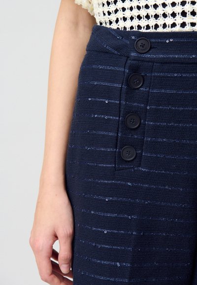 Jupe marine en tissu texturé, avec des rayures horizontales et quatre boutons noirs. De subtils sequins ajoutent un éclat à la surface du tissu.