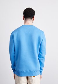 Felpa blu realizzata in misto cotone, con collo tondo e polsini a coste, presentando una piccola etichetta rettangolare sul retro.