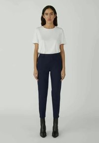 Witte T-shirt met korte mouwen, gecombineerd met marineblauwe slim-fit broek en zwarte instaplaarzen met hak, staand tegen een neutrale achtergrond.