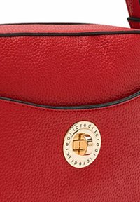 Bolso de piel roja texturizada con un cierre circular dorado y ribetes negros a lo largo de los bordes. Presenta una forma suave y redondeada.