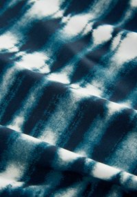 Tessuto blu e bianco con un texture liscia. Presenta onde orizzontali di colore che si mescolano, mostrando un effetto acquerello.