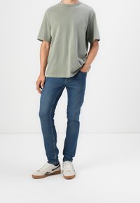 Camiseta verde claro de manga corta con escote redondo, combinada con jeans ajustados azules y zapatillas beige con acentos negros y suelas de goma.