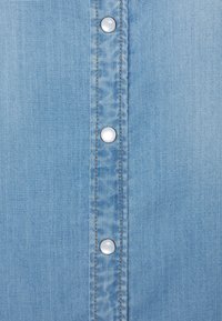 Lichtblauw denim overhemd met een verticale rij van vijf zilveren drukknoopjes. De stof heeft een subtiele textuur en contrasterende oranje stiksel.