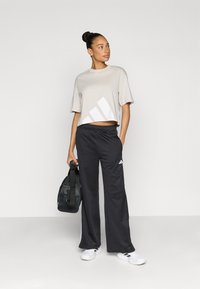 Šviesiai pilka trumpa marškinėliai su balta grafika, derinama su juodomis plačiomis kelnėmis. Komplekte – balti sportbačiai ir juodas sportinis maišelis.