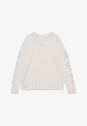 Mężczyzna ubrany w białą koszulę z długim rękawem z napisem, czarne spodenki, białe skarpetki, szare sneakersy i białe okulary przeciwsłoneczne, stojący na białym tle.