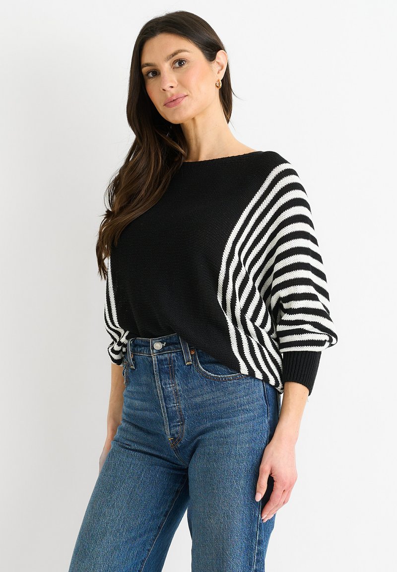 Maglione oversized a righe bianche e nere con maniche a pipistrello, abbinato a jeans di denim a vita alta, con un classico lavaggio blu.