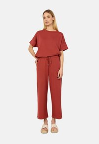 Red two-piece outfit featuring a loose-fitting top and drawstring pants, made of soft fabric with a relaxed silhouette. Worn with light sandals.