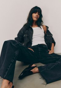 Črna denim oversize jakna in široke hlače, v kombinaciji z belo majico na tanko rame in črnimi čevlji. Hlače imajo raztrgane robove.