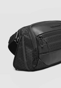 Borsello nero con motivo geometrico testurizzato, dettagli in pelle sintetica e molteplici scomparti con cerniera per la conservazione.