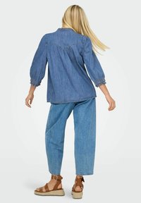 Camicia di jeans blu con maniche a sbuffo e polsini arricciati, abbinata a jeans a gamba larga azzurri e sandali espadrilles marroni.