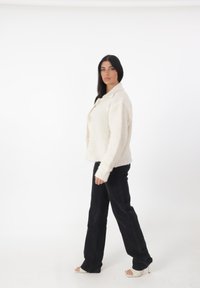 Chaqueta de forro polar texturizada color crema, con cuello de muesca y botones frontales, combinada con jeans de pierna ancha negros y tacones de tiras.