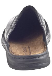 Chaussure noire à enfiler avec un bout arrondi, dessus en cuir et semelle intérieure en liège. Présente une texture lisse et des détails de couture le long du bord.