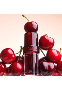 Bouteille en verre rouge avec une finition brillante, dotée d'un bouchon rouge foncé. Entourée de cerises brillantes et mûres sur un fond clair.