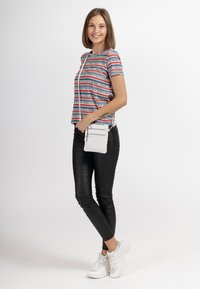 Maglietta a righe a maniche corte con testo rosso, bianco e blu, abbinata a pantaloni neri aderenti e sneakers bianche. Inclusa una piccola borsa a tracolla bianca.