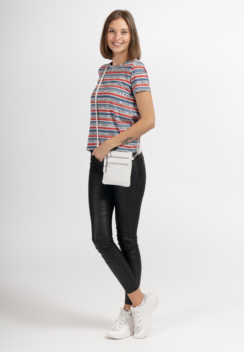 Striped short-sleeve tee with red, white, and blue text, paired with black fitted pants and white sneakers. Small white crossbody bag included.