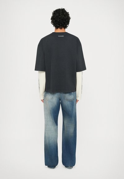 T-shirt nera oversize con collo rotondo e maniche corte, sovrapposta a una camicia bianca a maniche lunghe. Indossata con jeans chiari, strappi.