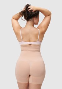 Beżowa bielizna modelująca o gładkiej fakturze, z regulowanymi cienkimi paskami i długością do połowy uda, zapewniająca bezszwowe dopasowanie do ciała.