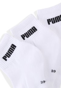 Białe skarpetki sportowe z żebrowanym mankietem, czarnym logo "PUMA" na każdej skarpetce oraz czarnymi oznaczeniami rozmiaru w okolicy palców.