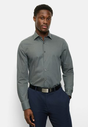 Button-up shirt in dark blue with circular pattern; long sleeves, classic collar, and black belt; paired with navy trousers.