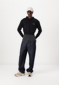 Svart cropped hoodie med logo, grå ribbet lag under, mørkeblå vid bukse og beige joggesko med kremfargede detaljer. Lys farget caps.