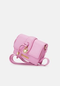 Růžová crossbody taška z umělé kůže se zlatým srdíčkovým zámkem, nastavitelným popruhem a embosovaným označením na přední straně.