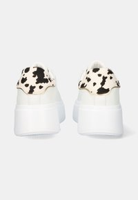 Zapatillas blancas con una suela gruesa, con un talón de tela a lunares en blanco y negro. Parte superior lisa y diseño de puntera redonda.