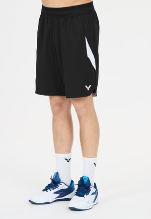 Mand iført sorte sportsshorts med hvide sidelommer, hvide kælængde sokker og hvide og blå atletiksko på hvid baggrund.