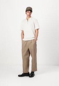 Beige short-sleeve polo with zippered neck; relaxed-fit tan trousers; black shoes; brown plaid cap. Minimalistic design with clean lines.