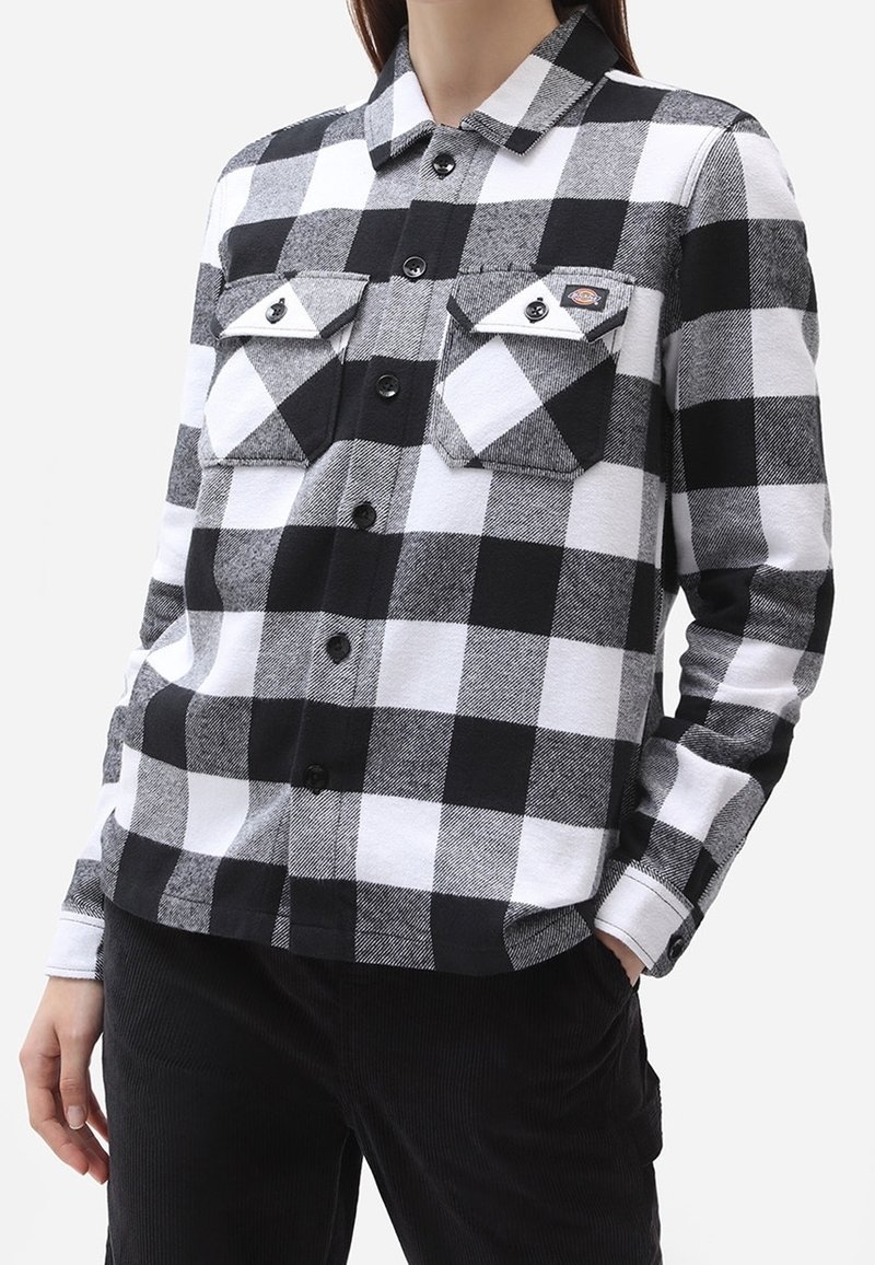 Czarna i biała koszula flanelowa w kratę z długimi rękawami, z przodu zapięcie na guziki, dwie kieszenie na piersi i teksturowana tkanina.