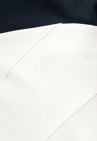 Nahaufnahme von gefaltetem weißem Stoff mit einer diagonalen Falte vor einem schwarzen, strukturierten Hintergrund.