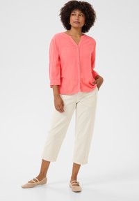 Camicia rosa corallo con scollo a V e maniche a tre quarti, abbinata a pantaloni cropped crema e ballerine in rete beige. Texture liscia.