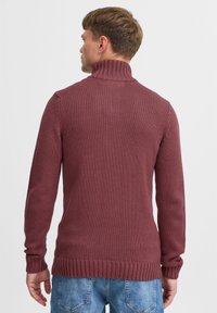 Bordeaux-roter gestrickter Pullover mit hohem Kragen, gerippten Bündchen und Saum. Ausgestattet mit einer strukturierten Webart, von hinten mit einer lockeren Passform gezeigt.