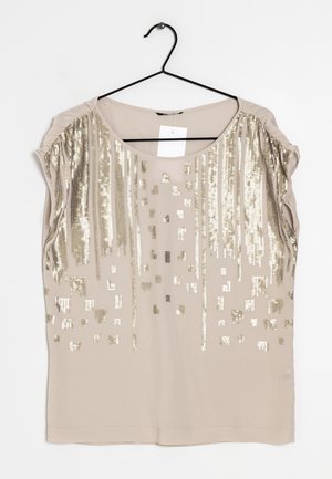 Blouse beige sans manches avec encolure ronde, décorée de sequins dorés verticaux et carrés, suspendue sur un cintre noir.