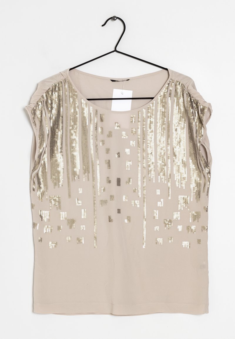 Blouse beige sans manches avec encolure ronde, décorée de sequins dorés verticaux et carrés, suspendue sur un cintre noir.