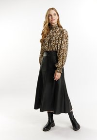 Langarmige blouse met hoge kraag en een bloemenpatroon, gecombineerd met een zwarte leren rok met knoopsluiting aan de voorkant. Zwarte enkellaarzen maken de look af.