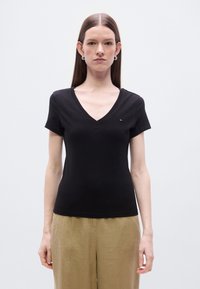 Μαύρο βαμβακερό μπλουζάκι με λαιμόκοψη σε σχήμα V και κοντά μανίκια, με ένα μικρό κεντημένο λογότυπο στο αριστερό στήθος. Ομαλή υφή.